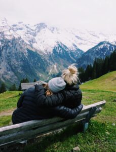 2 Females hugging on a bench in front of a mountain range in Switzerland