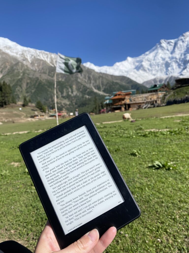 Reading on a Kindle in front of a beautiful Mountain Range in Pakistan