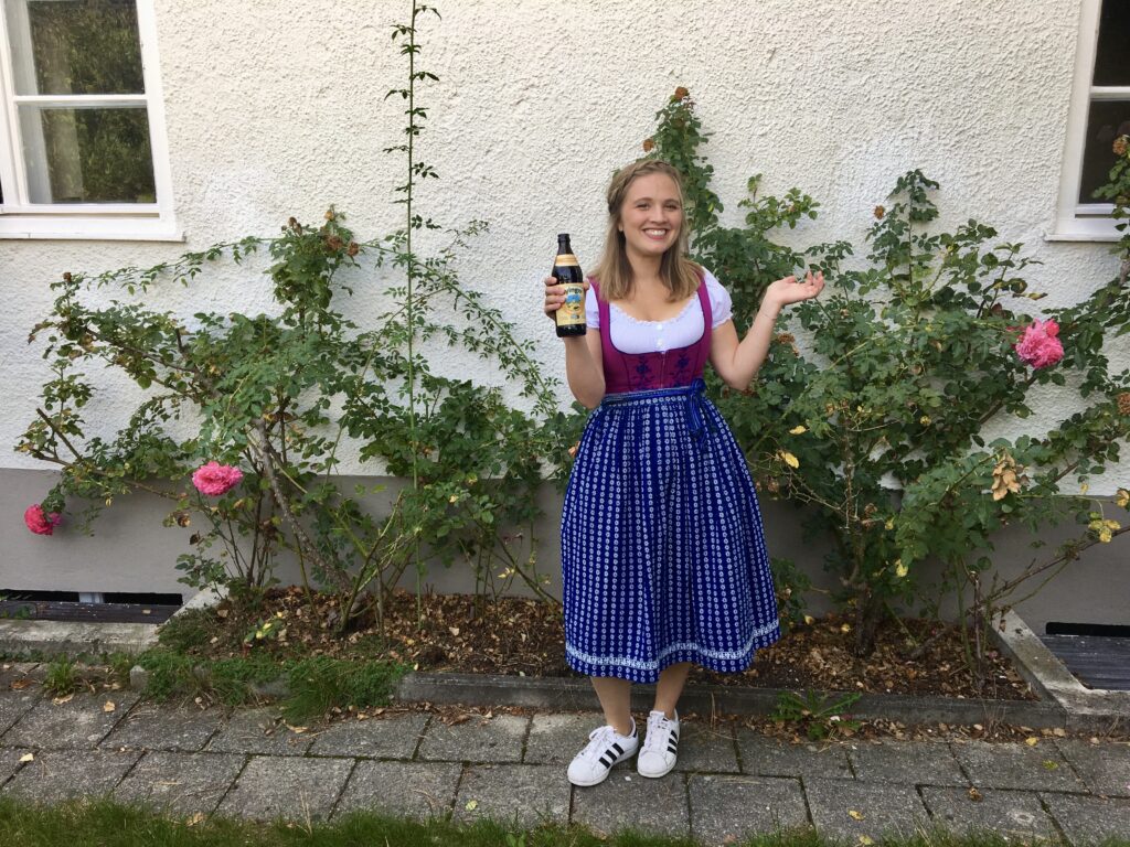 Mariah in front of a house wearing a pink and blue Traditional Dirndl in Munich Germany