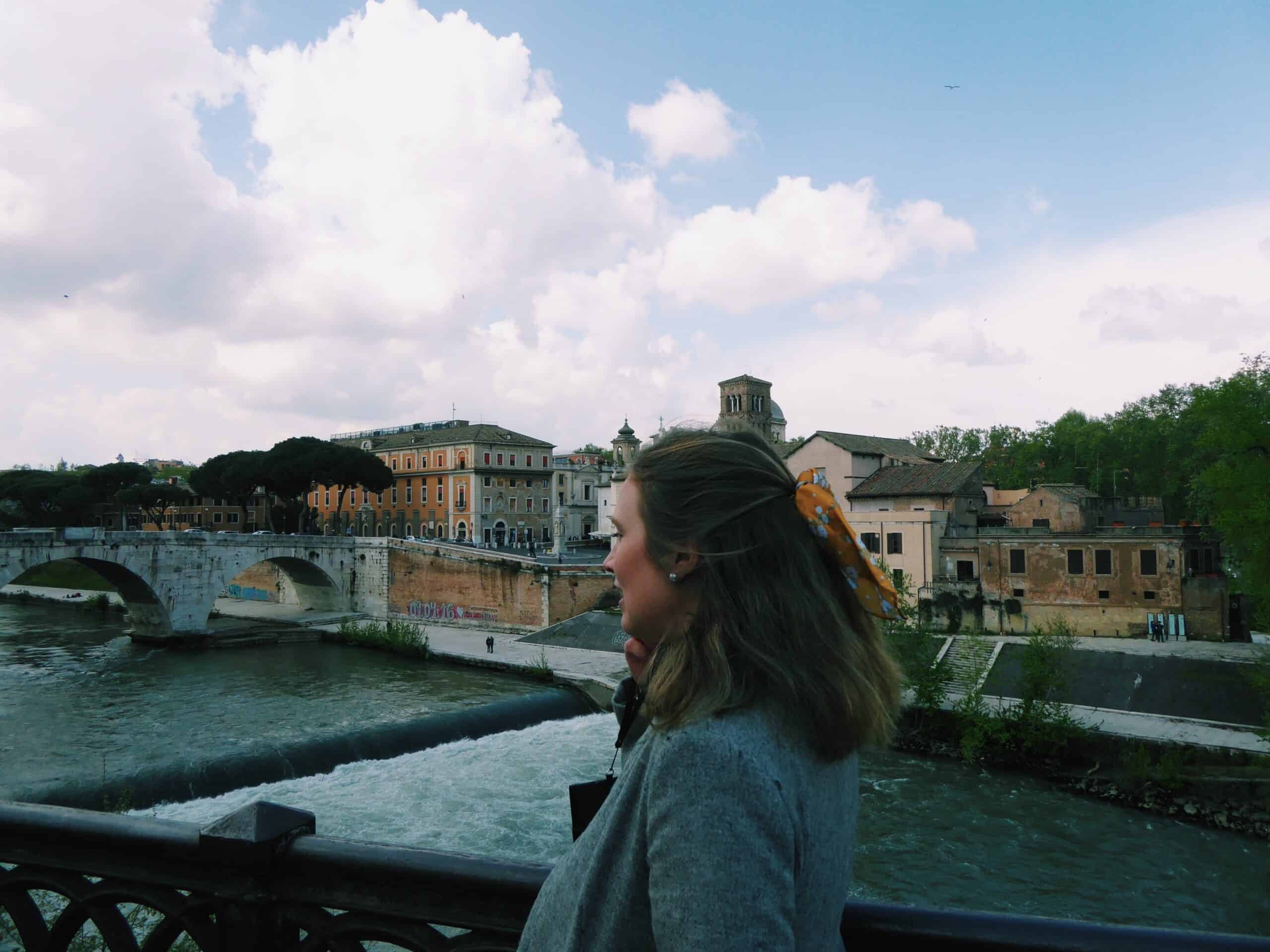 Photo of Mariah, 20 something year old female, near a bridge in Rome, Italy with beautiful Italian architecture buildings in the background.